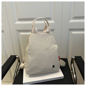 Detail of cream white canvas backpack featuring red side tag and minimalist metal logo