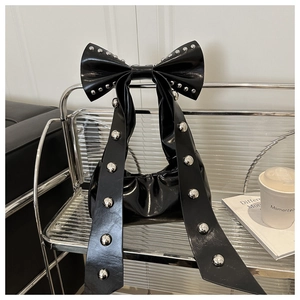 Détail du sac bandoulière en cuir verni noir avec grand nœud et rivets argentés brillants