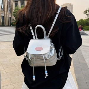 Silver mini backpack with pink logo and beaded drawstring shown in an outdoor street view
