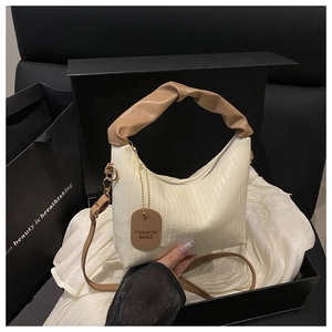 Detail of off-white pleated bucket bag with brown handles in luxury gift box packaging