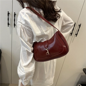 Elegant wine red patent leather shoulder bag with gold clasp on white lace shirt
