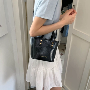 Elegant black glossy leather bucket bag with gold rivets and shoulder strap for women