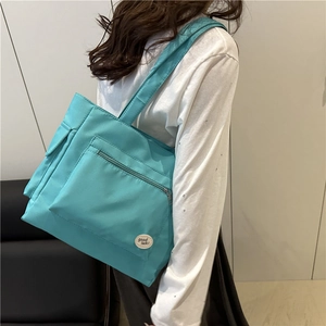 Grand sac fourre-tout en nylon cyan avec poche zippée et écusson porté par un mannequin
