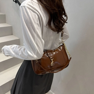 Sac bandoulière en cuir verni marron avec détails dorés porté par un mannequin