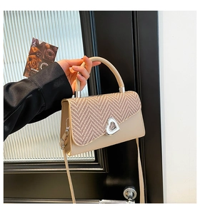 Detail of beige crossbody bag with woven flap and silver heart-shaped twist lock