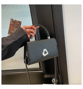 Detail of black crossbody bag with silver heart-shaped clasp and textured faux leather finish