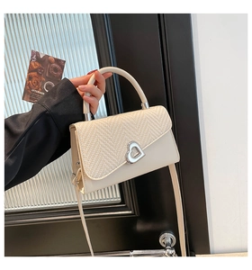 Detail of cream white bag showing woven flap, silver heart lock, and sturdy top handle