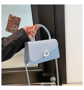 Detailed close-up of light blue woven leather crossbody bag with heart shaped silver lock