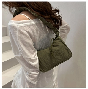 Olive green nylon shoulder bag with pleated strap detail shown on a model's shoulder