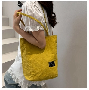 Detail of yellow nylon tote bag with brand patch and wrinkled texture on shoulder strap
