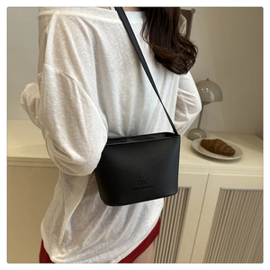 Close-up of black litchi grain bucket bag showing the embossed logo and slim strap