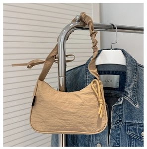 Detail of beige nylon pleated shoulder bag with knotted cloud-style strap hanging on rack
