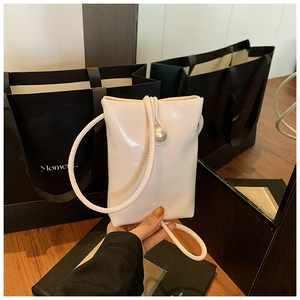 Close-up of a minimalist beige crossbody bag featuring a glossy finish and pearl detail