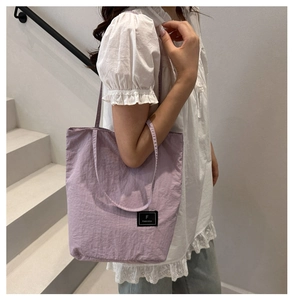Detail shot of purple nylon tote bag with brand label against a minimalist white stairs background