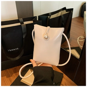 Detail of cream rectangular bag with large pearl clasp and thin rope shoulder strap