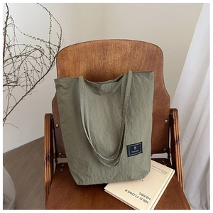 Olive green canvas tote bag with black logo label placed on a rustic wooden chair