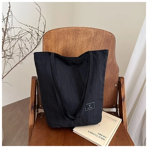Detail of minimalist black canvas bucket bag with logo tag on a rustic wooden chair