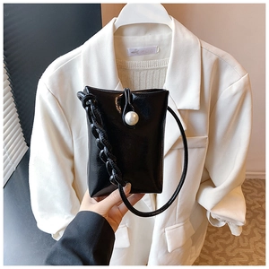 Detail of black glossy handbag with oversized white pearl and thick chain strap