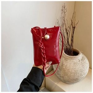 Detail of red patent leather crossbody bag featuring a large pearl clasp and woven strap