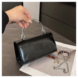Detail der schwarzen Lackhandtasche mit silbernem Metallringgriff und Logoprägung