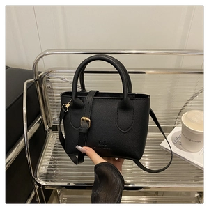 Detail of black litchi grain leather crossbody bag with DX logo and gold buckle