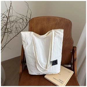 Detail of off-white canvas tote bag featuring a brand logo on a vintage wooden chair
