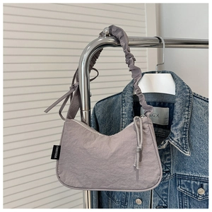 Detail of lavender pleated shoulder bag with long knot zipper pull on a metal rack
