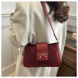 Close-up of red lychee leather shoulder bag with a gold metal bow on cream blazer