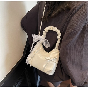 Close-up of stylish off-white crossbody bag featuring a lace bow and ruffled handle