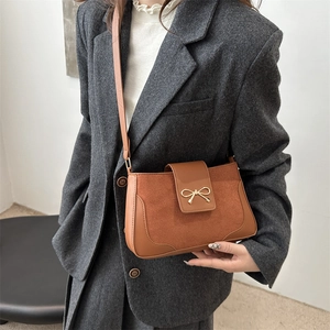 Brown leather crossbody bag with gold bow detail, styled on a grey suit jacket