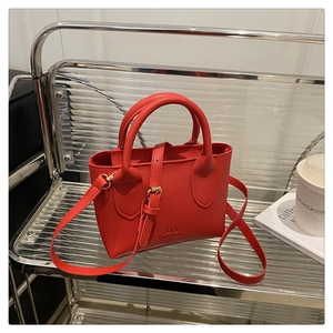 Close-up of red pebbled leather crossbody bag with logo detail on an elegant chair