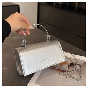 Detailaufnahme einer silbernen Metallic-Umhängetasche mit großem Rundgriff und Metallkette