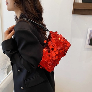 Red sequin underarm bag with black shoulder strap worn by a model in a black blazer