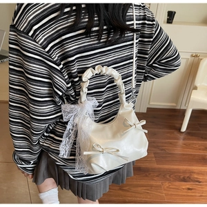 Detailed view of a cream pleated shoulder bag with large white lace bows and leather details
