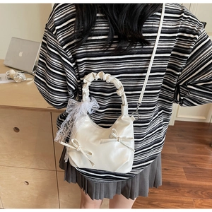 Detail of white shoulder bag with bow accents, lace ribbon and ruched handle design