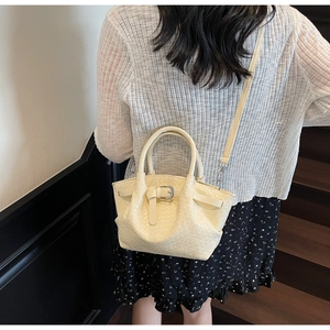 Détail du sac seau tressé crème montrant la texture et la bandoulière sur modèle