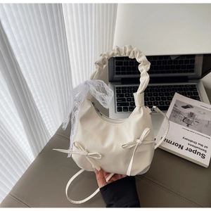 Detail of off-white hobo bag with bow accents and ruffled handle in a home office setting
