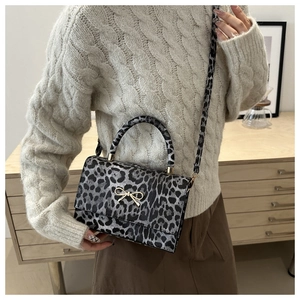Close-up of stylish leopard print square bag with golden bow and top handle