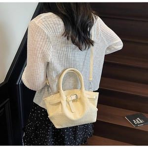 Détail d'un sac seau beige tissé avec boucle argentée et bandoulière sur un escalier