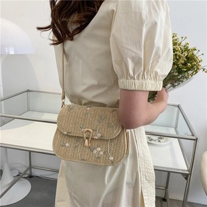 Sac bandoulière en paille avec broderie florale et fermoir métallique porté par un mannequin