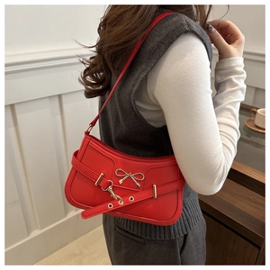 Detail of red leather shoulder bag featuring a gold bow and decorative metal eyelet strap