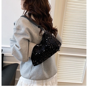 Close-up of black sequined shoulder bag with leather strap worn by a model in casual style