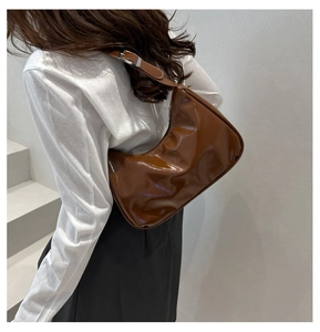 Close-up of brown glossy patent leather hobo bag with adjustable silver buckle strap