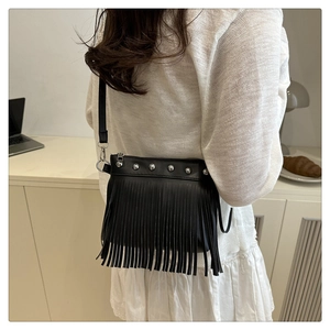 Détail du sac bandoulière noir à franges avec rivets porté dans un bureau contemporain