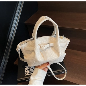 Détail d'un sac seau blanc en cuir tressé avec boucle métallique sur fond en bois