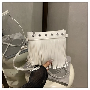 Détail d'un sac blanc à franges avec clous argentés et pompons sur une surface miroir