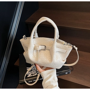 Détail d'un sac seau tressé blanc crème avec boucle en métal sur fond urbain minimaliste