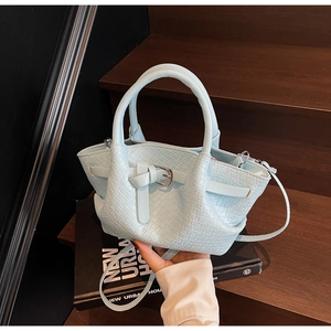 Gros plan d'un sac seau en cuir tressé bleu clair avec bandoulière sur bois sombre
