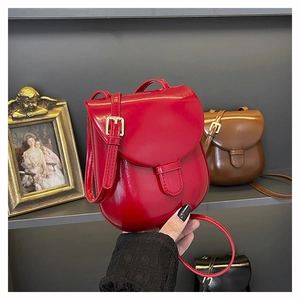 Detail of a red patent leather mini crossbody bag with gold buckle and adjustable strap