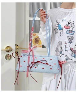 Close-up of light blue shoulder bag with red bows, heart charm, and lace ribbon detail